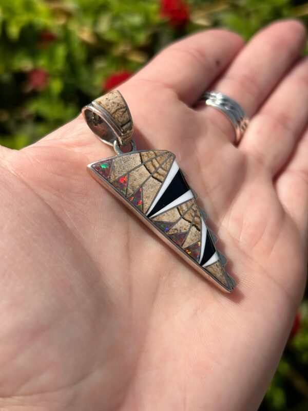 A silver pendant with colorful inlays in hand.