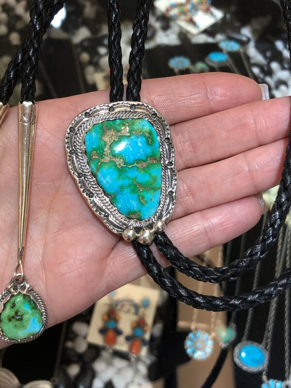 A person is holding a necklace with turquoise stones and black leather.