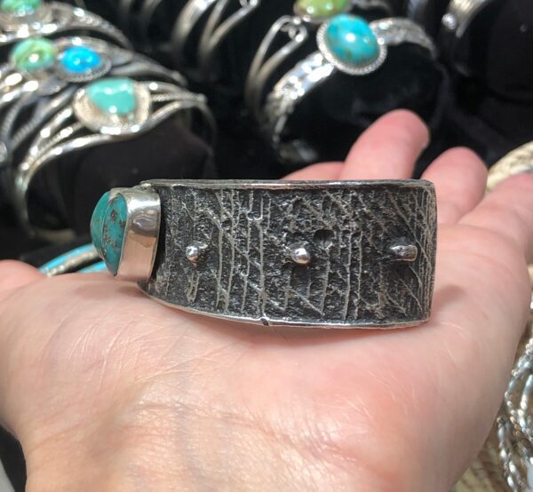 A person is holding a silver cuff with turquoise stones.