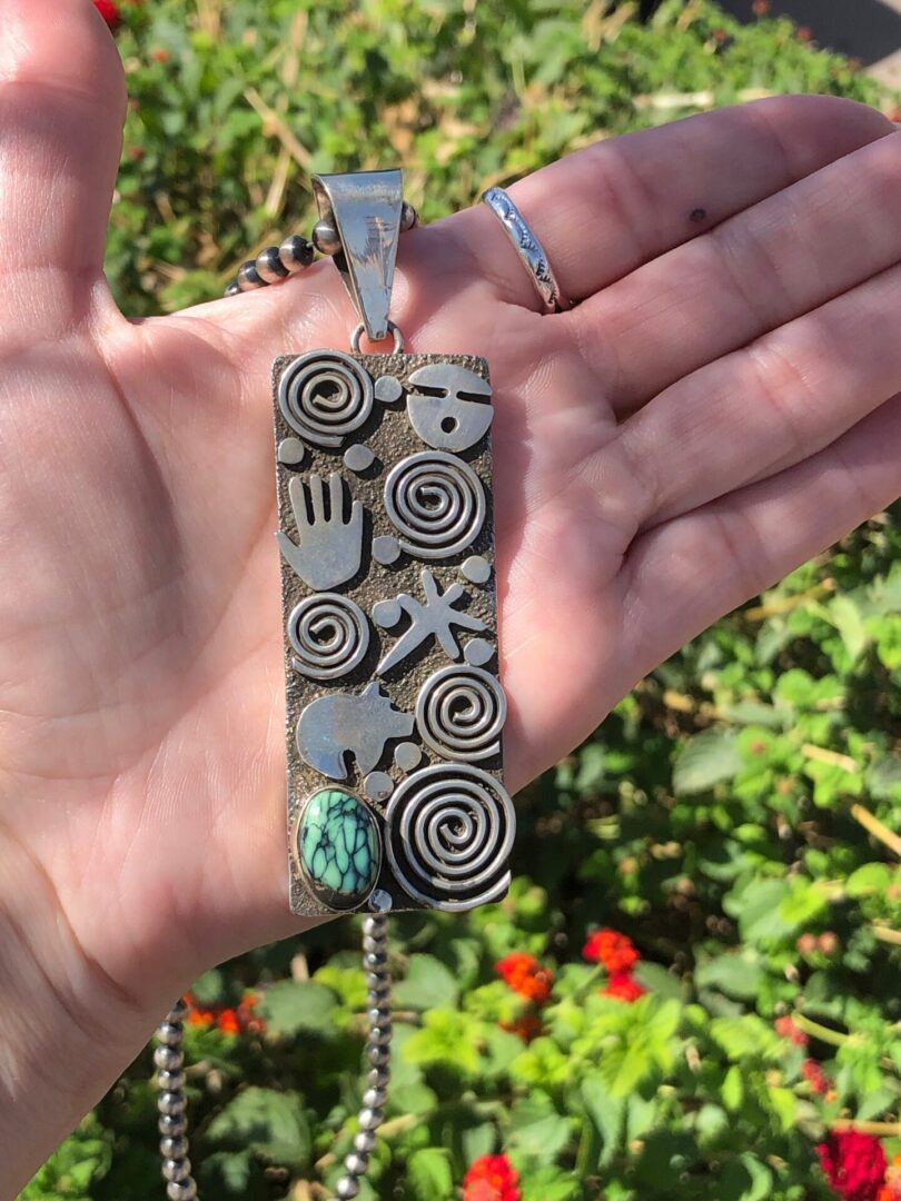 A hand holding a silver pendant with a turquoise stone.