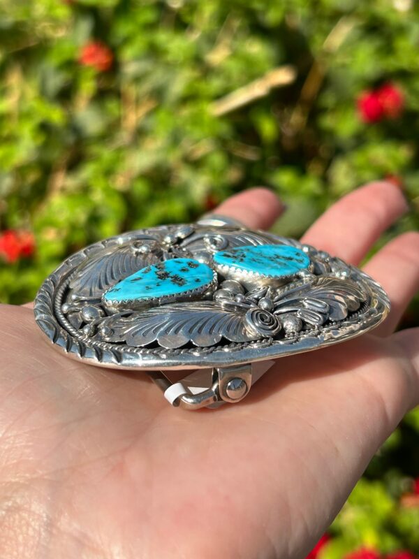 A person holding a silver belt buckle with turquoise stones.