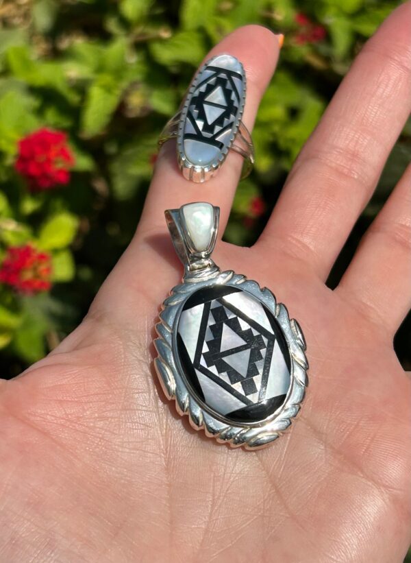 A hand holding a silver ring and pendant with black and white inlay.