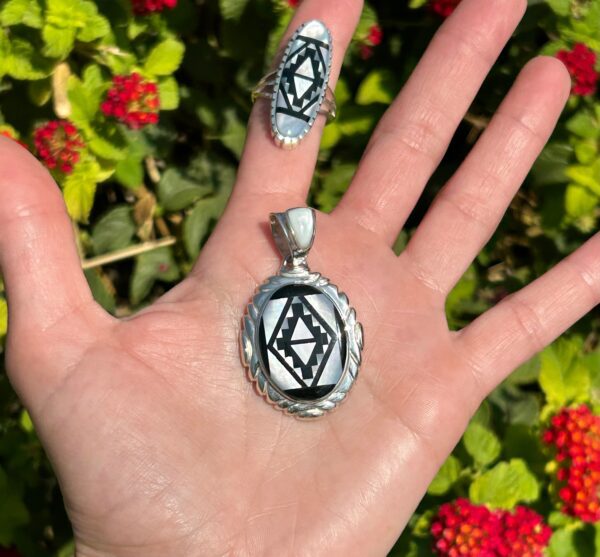 A hand holding a silver and black pendant and ring.