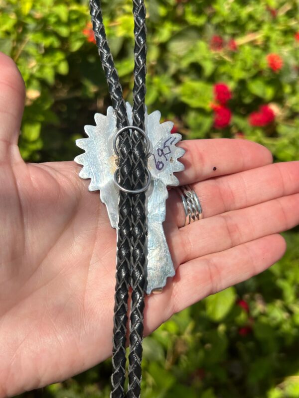 A person is holding a black and silver necklace with a flower on it.