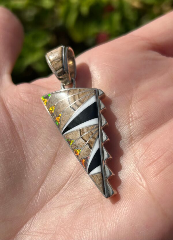 A silver pendant with colorful inlay in the shape of a shark tooth.