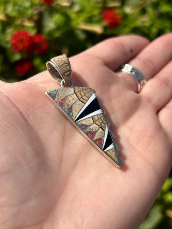 A hand holding a silver pendant with colorful inlays.