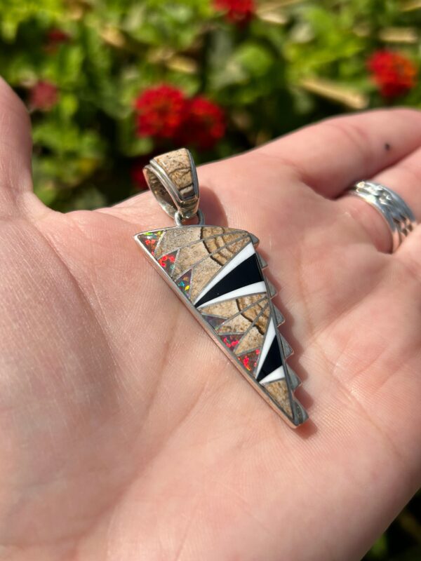 A silver pendant with colorful inlay in hand.