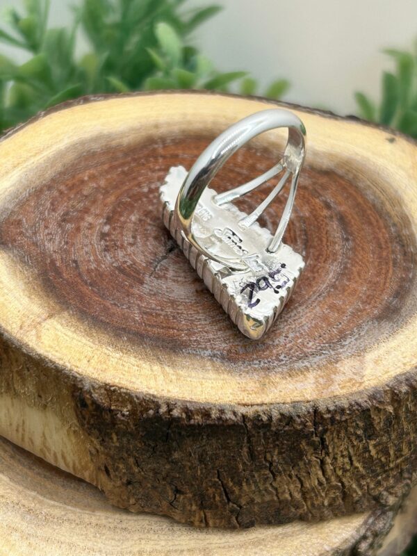 A silver ring with green stones on wood.