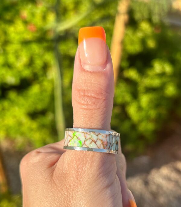 A person is modeling a silver ring with colorful inlays.