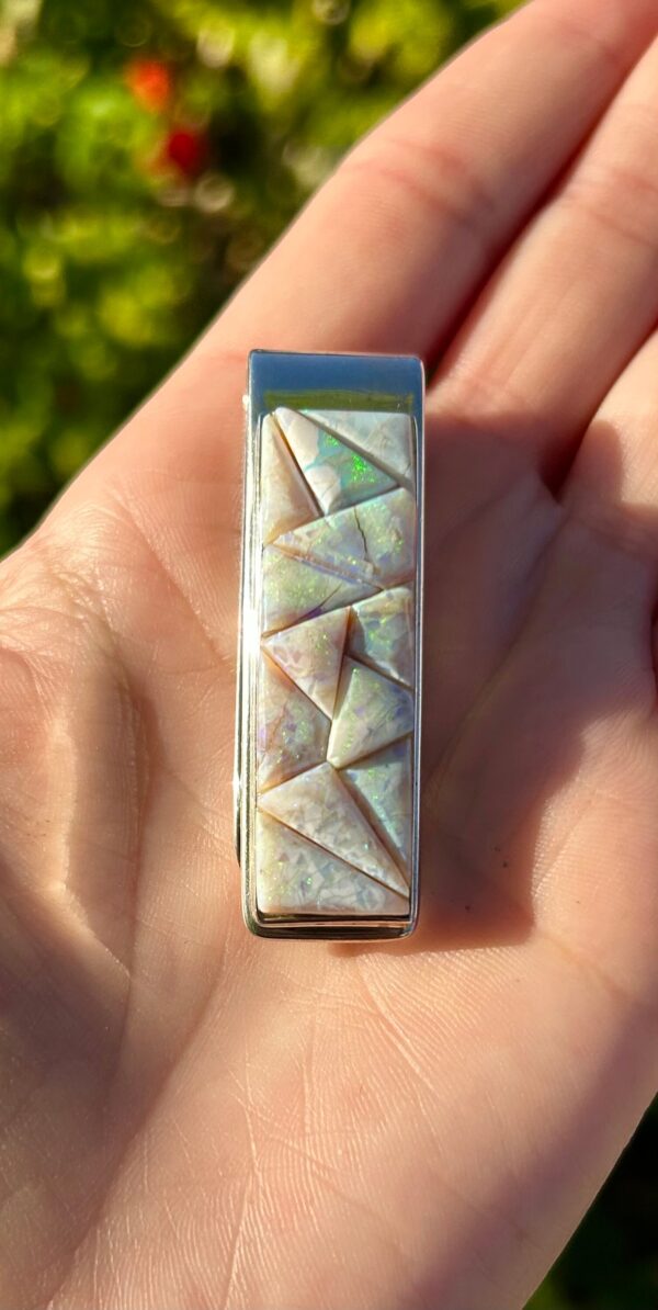 A hand holding a silver and white opal money clip.