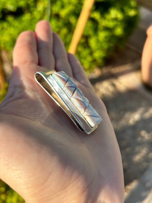 A hand holding a silver and mother-of-pearl money clip.