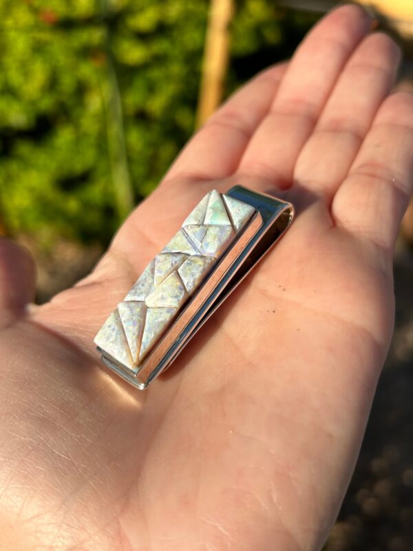 A hand holding a silver money clip with an opal inlay.