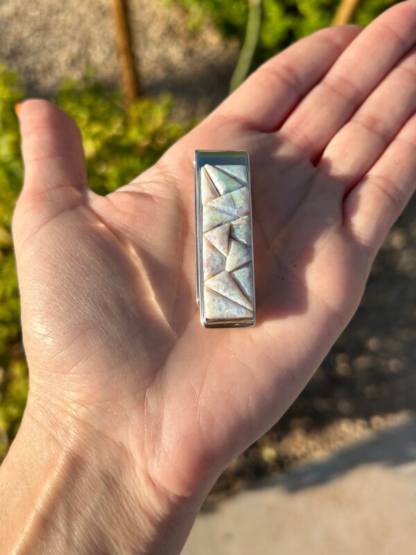 A hand holding a silver and opal money clip.