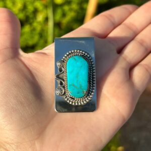 A hand holding a silver money clip with a turquoise stone.