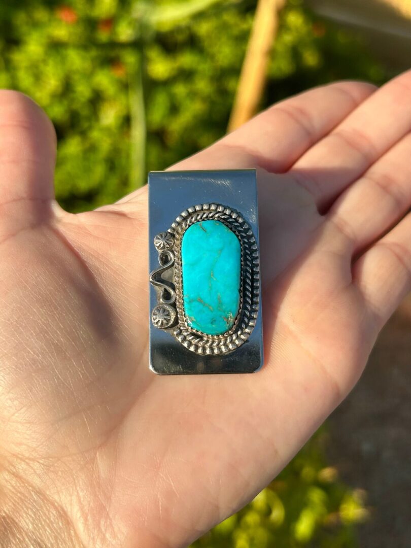 A hand holding a silver money clip with a turquoise stone.