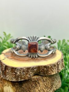 A silver bracelet with a red stone on it.