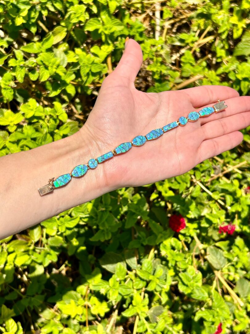 A person's hand holding a blue opal bracelet.