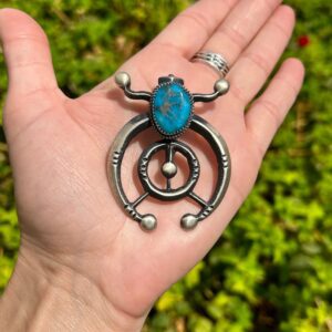 A person holding a necklace with a turquoise stone in it.