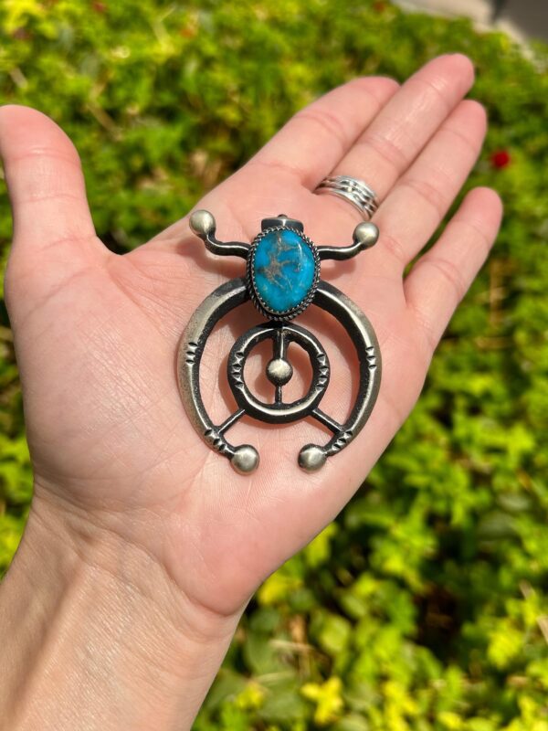 A person holding a necklace with a turquoise stone in it.