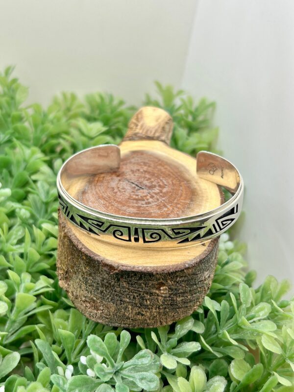 A silver cuff bracelet sitting on top of a piece of wood.