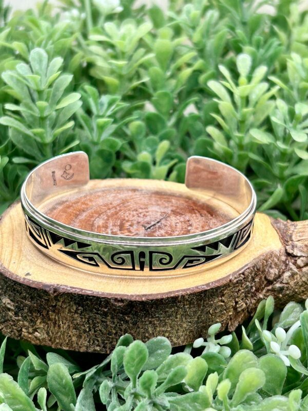 A silver cuff bracelet sitting on top of a piece of wood.