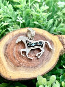 A silver horse pendant on top of a piece of wood.