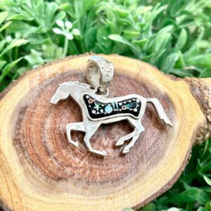 A silver horse pendant on top of a piece of wood.