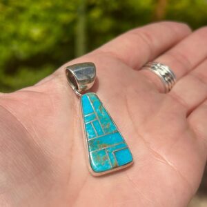 A hand holding a turquoise stone pendant.