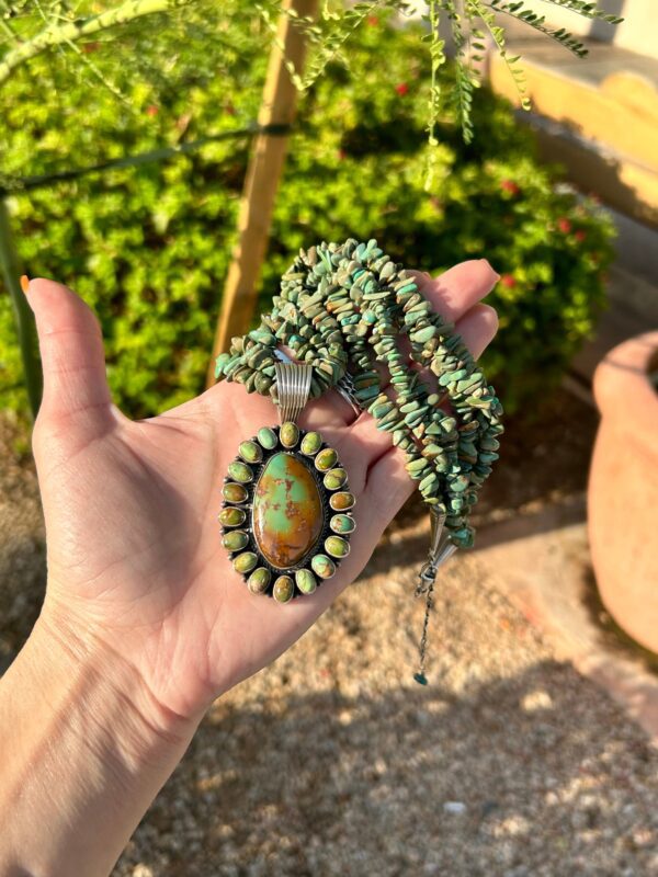 A hand holding a turquoise and silver necklace.