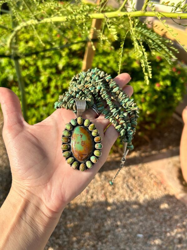 A hand holding a turquoise and silver necklace.