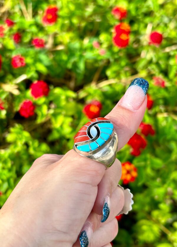 A hand wearing a silver ring with red, white, and blue stones.