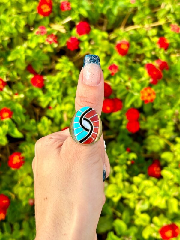 A hand wearing a silver ring with blue and red stones.