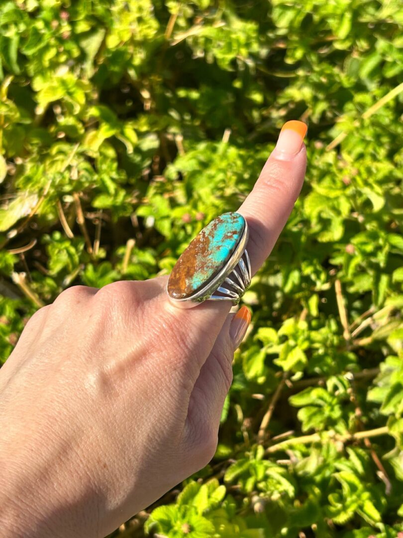 A person holding a ring with a turquoise stone.