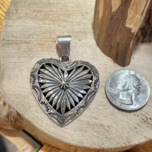 A silver heart shaped pendant next to a dime.