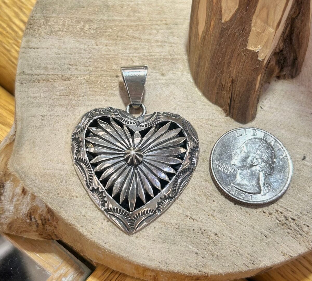 A silver heart shaped pendant next to a dime.