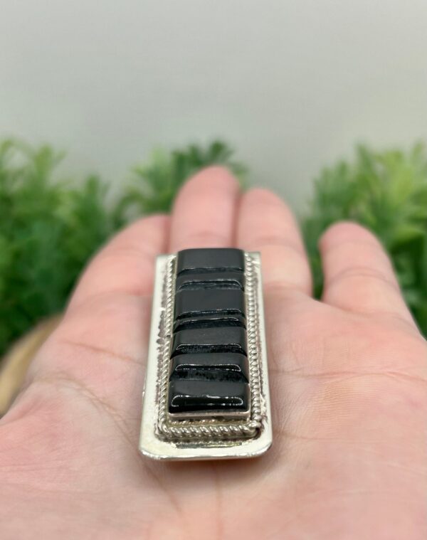 A hand holding a silver and black tie clip.