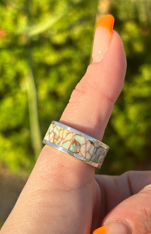 A woman's thumb wearing a silver ring with colorful inlays.