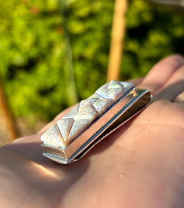 A hand holding a silver money clip with an opal inlay.