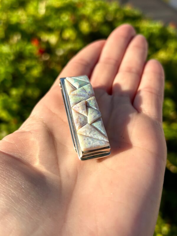 A hand holding a silver and opal tie clip.