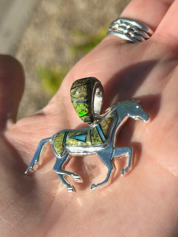 A silver horse pendant with green and blue gemstones.