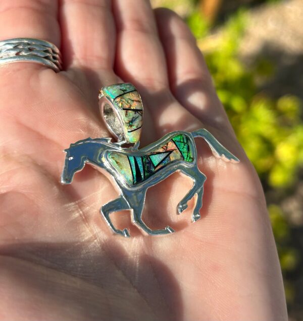 A silver horse pendant with green and blue inlay.