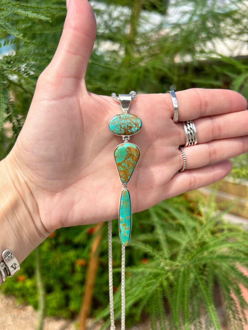A hand holding a necklace with three turquoise stones.