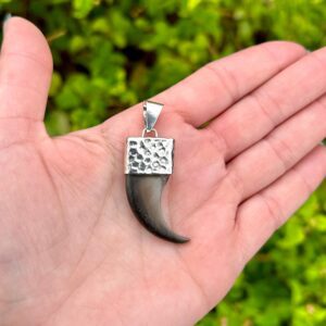A hand holding a silver tiger tooth pendant.