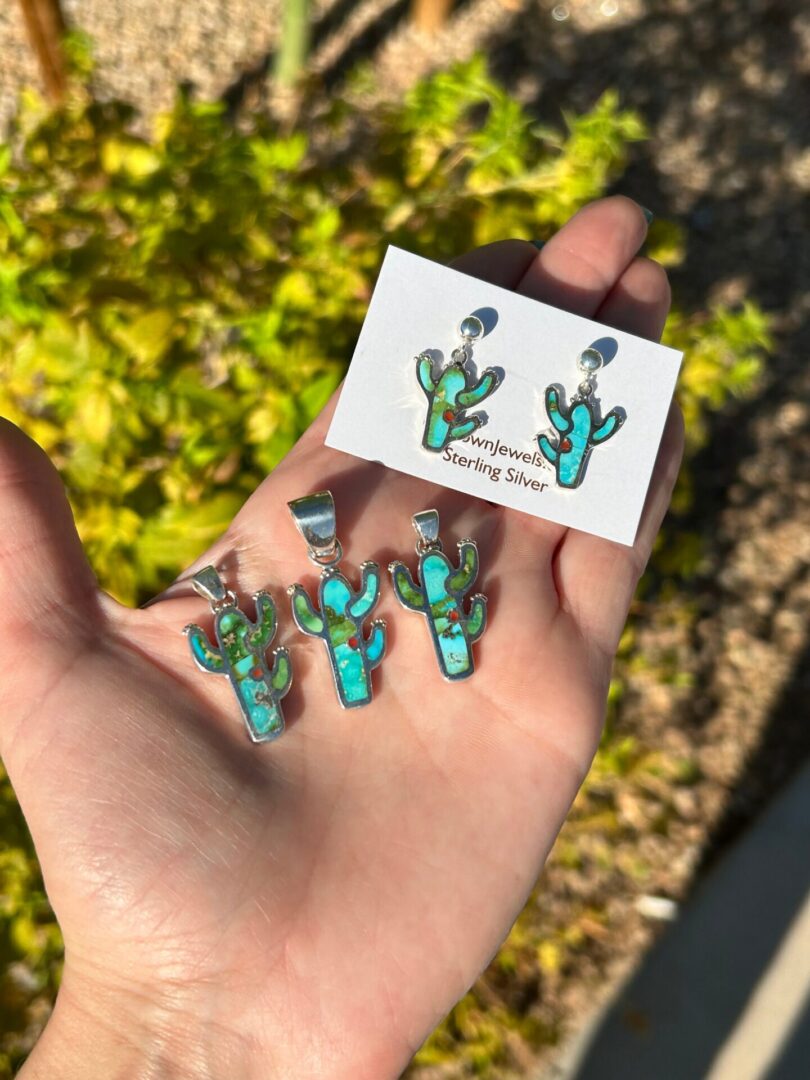 A person holding a pair of turquoise cactus earrings and a card.