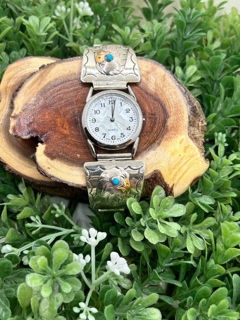 A silver and turquoise watch sitting on a piece of wood.