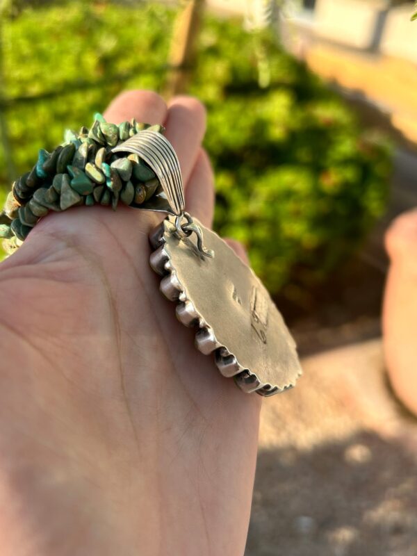 A hand holding a silver pendant with turquoise stones.