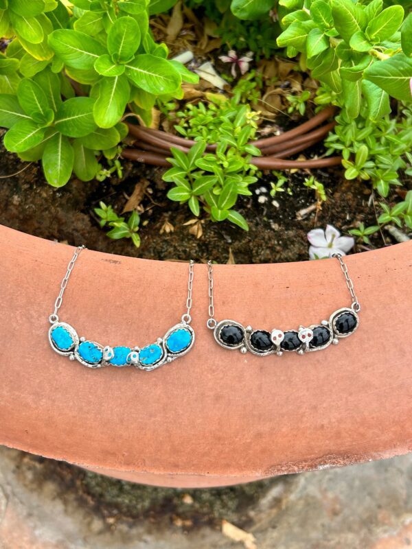Two necklaces with black and turquoise stones on top of a potted plant.