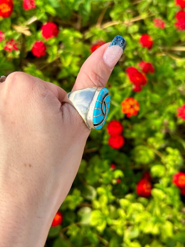 A hand wearing a silver ring with a blue stone.