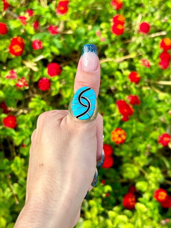 A hand wearing a silver ring with blue stone.