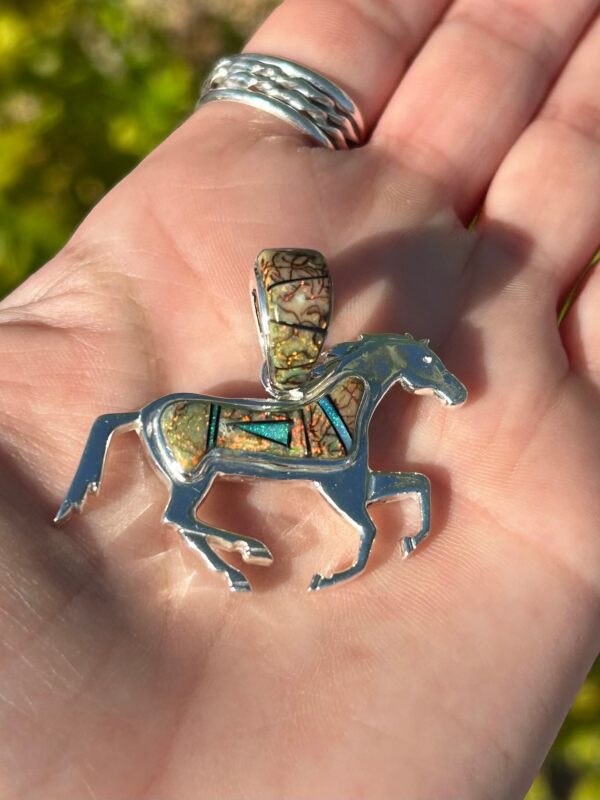 A silver horse pendant with blue and green stones.